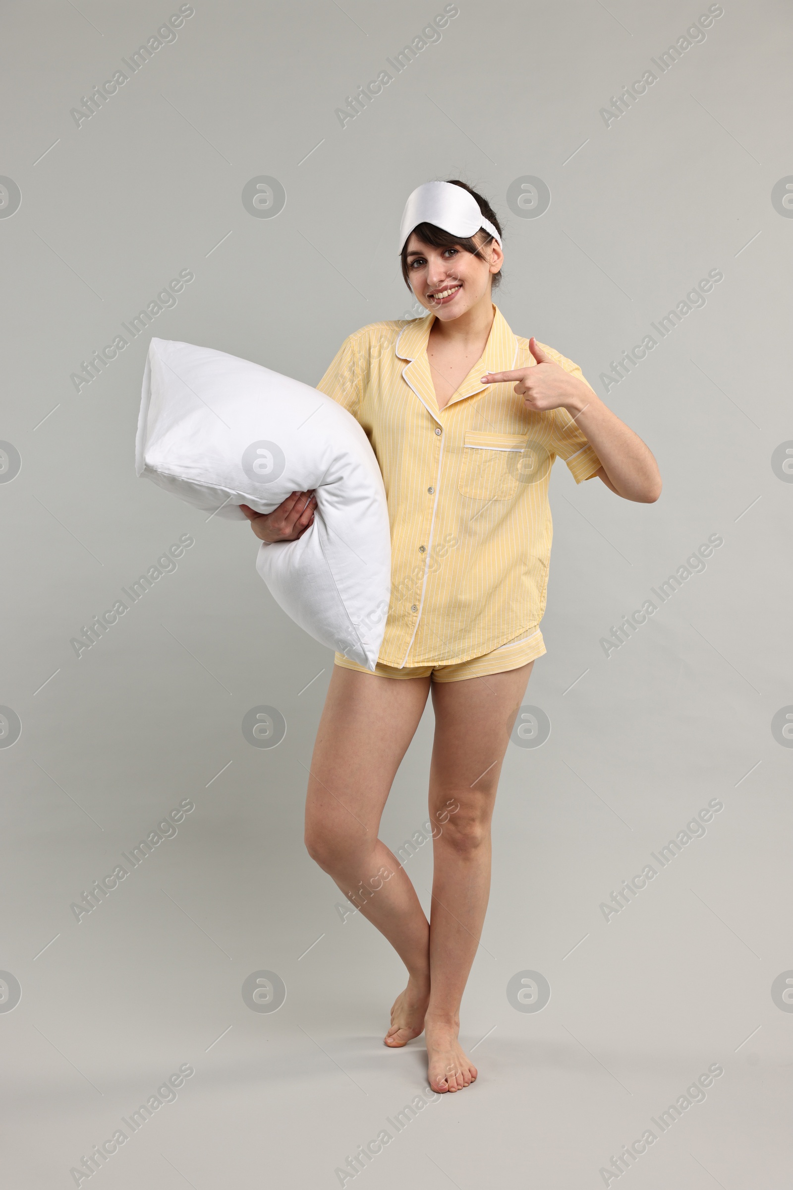 Photo of Happy woman in pyjama and sleep mask holding pillow on grey background