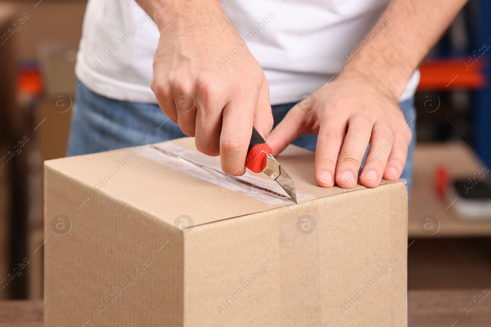 Photo of Post office worker with utility knife opening parcel indoors, closeup