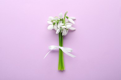 Photo of Beautiful bouquet of snowdrops on lilac background, top view