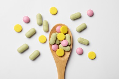 Photo of Different vitamin pills in wooden spoon on white background, top view