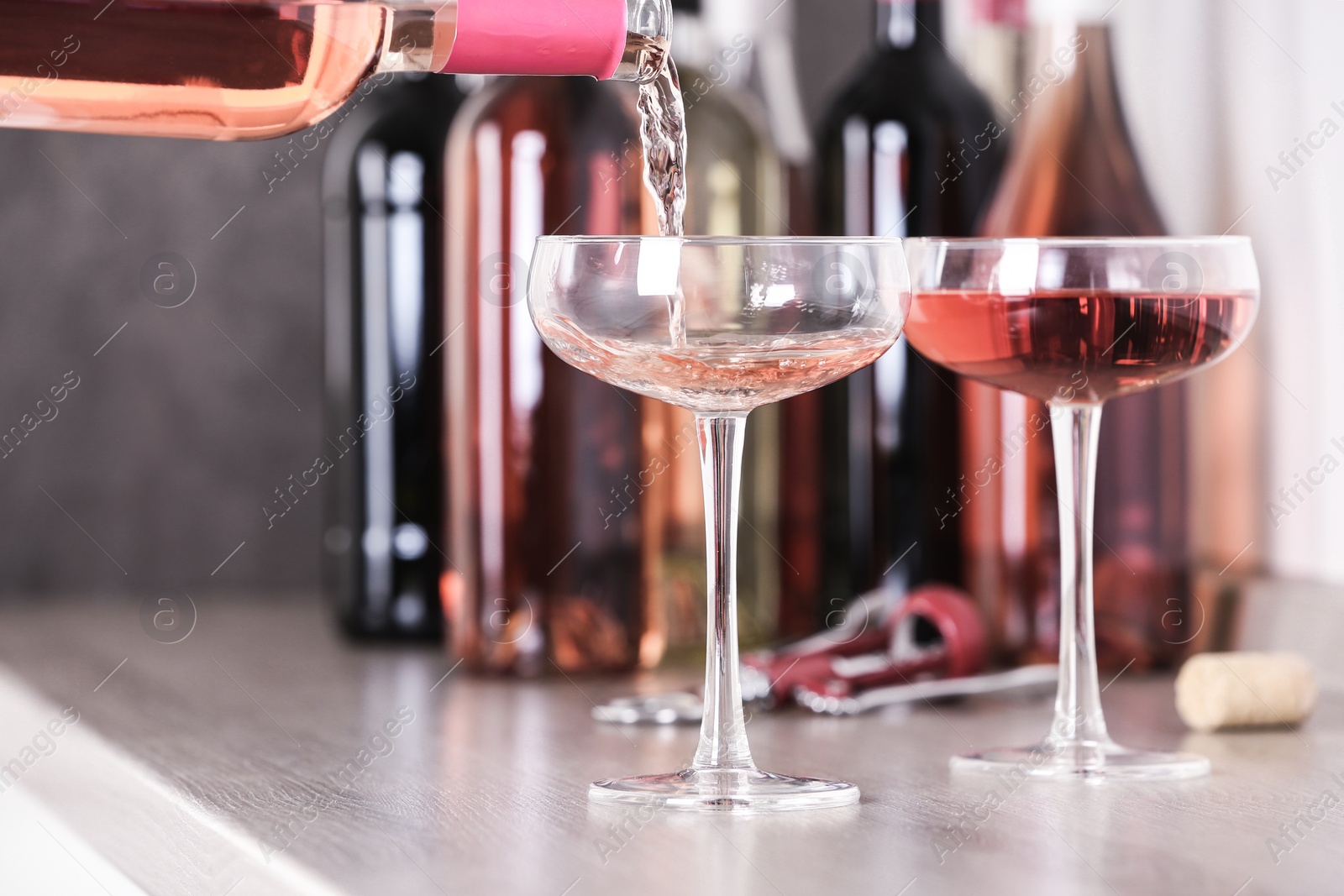 Photo of Pouring delicious rose wine from bottle into glass on wooden counter, closeup