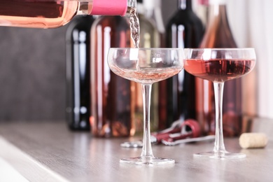 Pouring delicious rose wine from bottle into glass on wooden counter, closeup