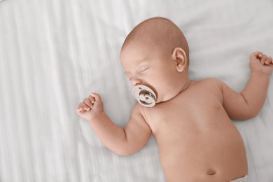 Photo of Cute little baby with pacifier sleeping on bed, top view