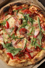 Photo of Tasty pizza with cheese, tomato and arugula in cardboard box on table, top view