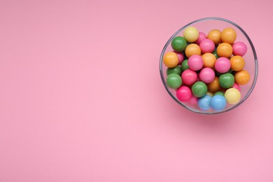 Photo of Bowl with many bright gumballs on pink background, top view. Space for text