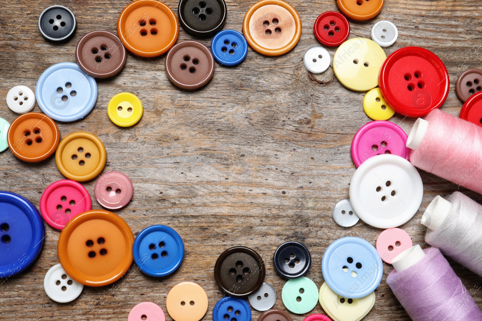 Photo of Frame made of buttons and threads on wooden background, top view. Tailoring equipment