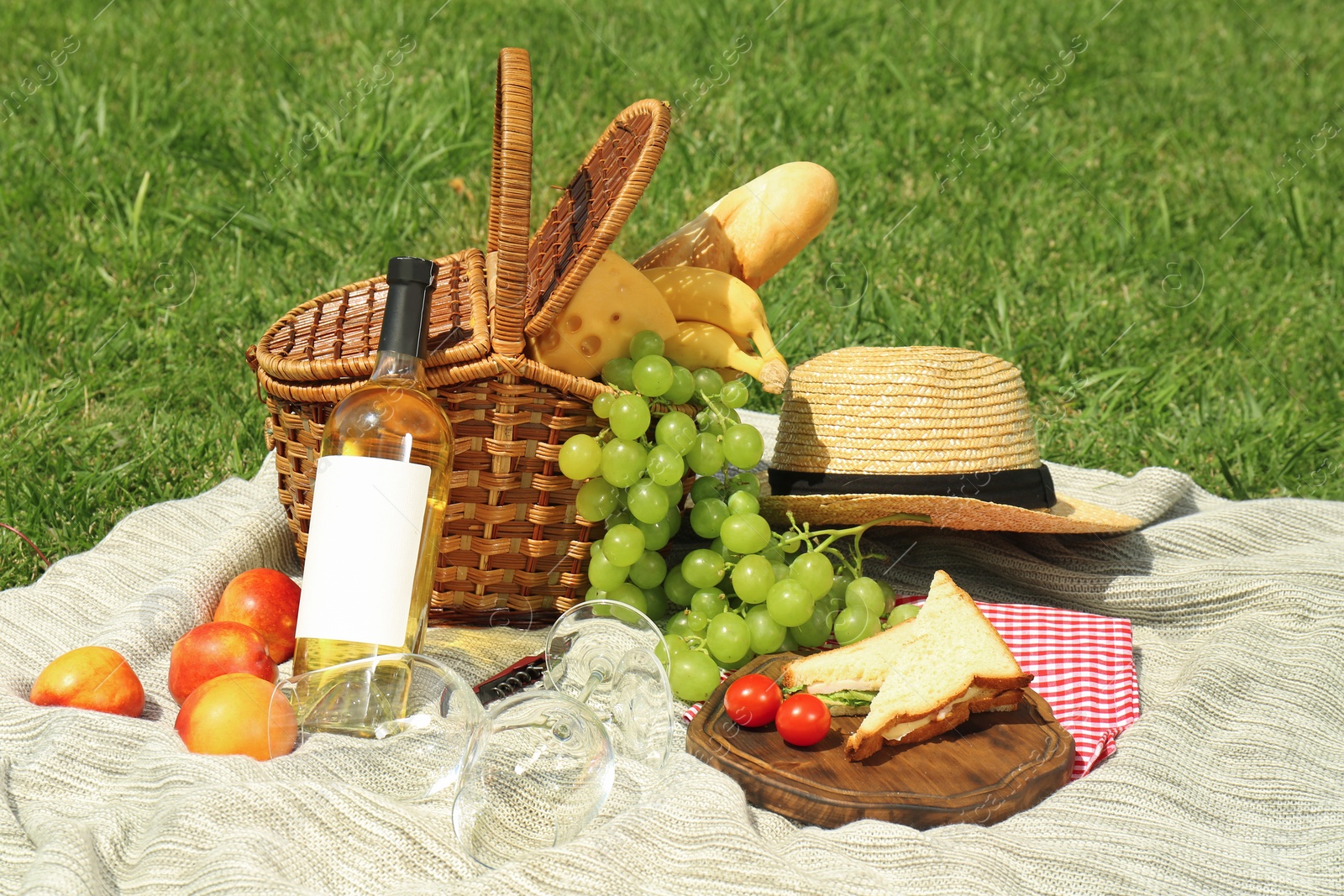 Photo of Basket with food and straw hat on blanket in park. Summer picnic