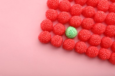 Photo of Delicious green gummy raspberry candy among red ones on pink background, flat lay. Space for text