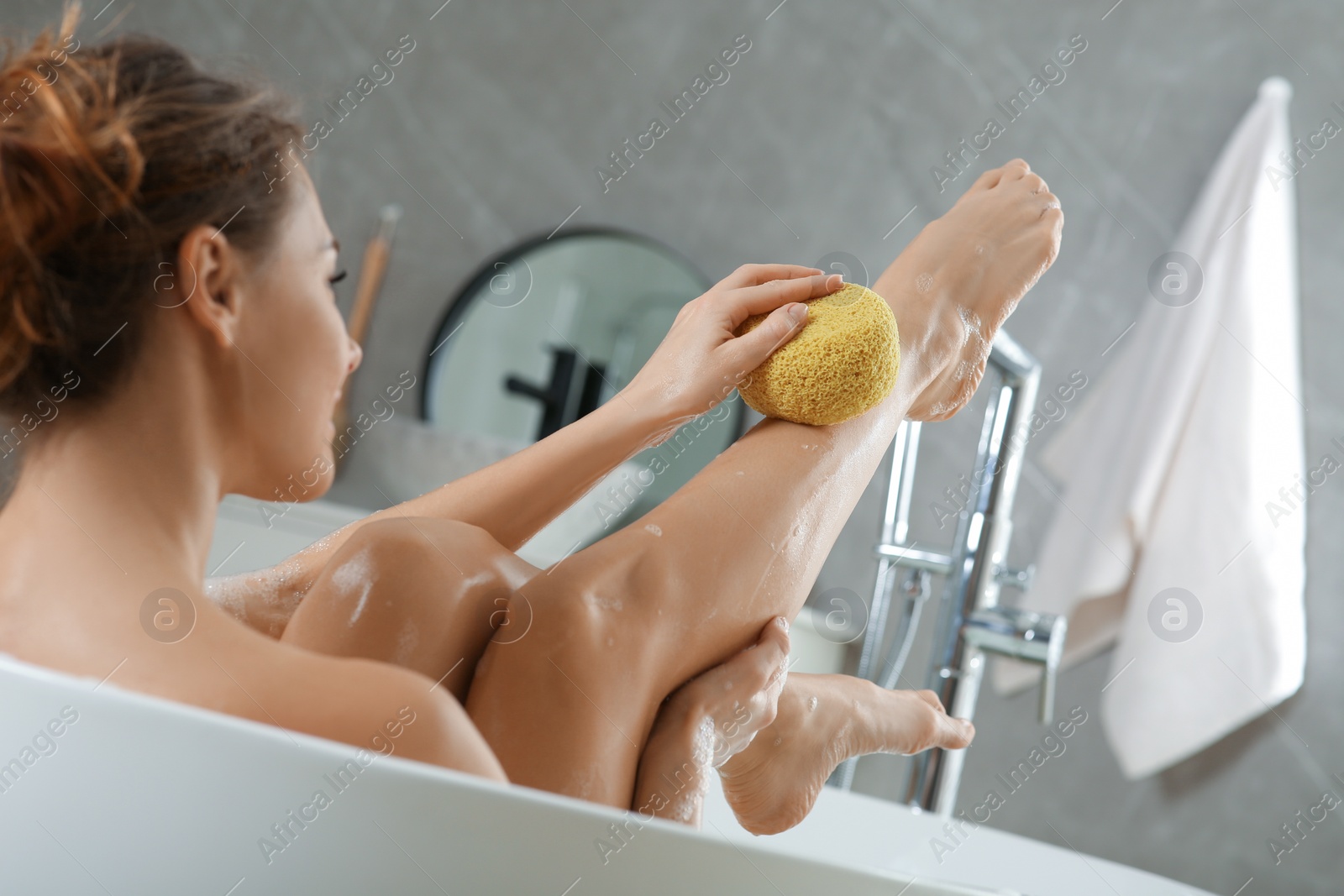 Photo of Beautiful woman with sponge taking bath indoors