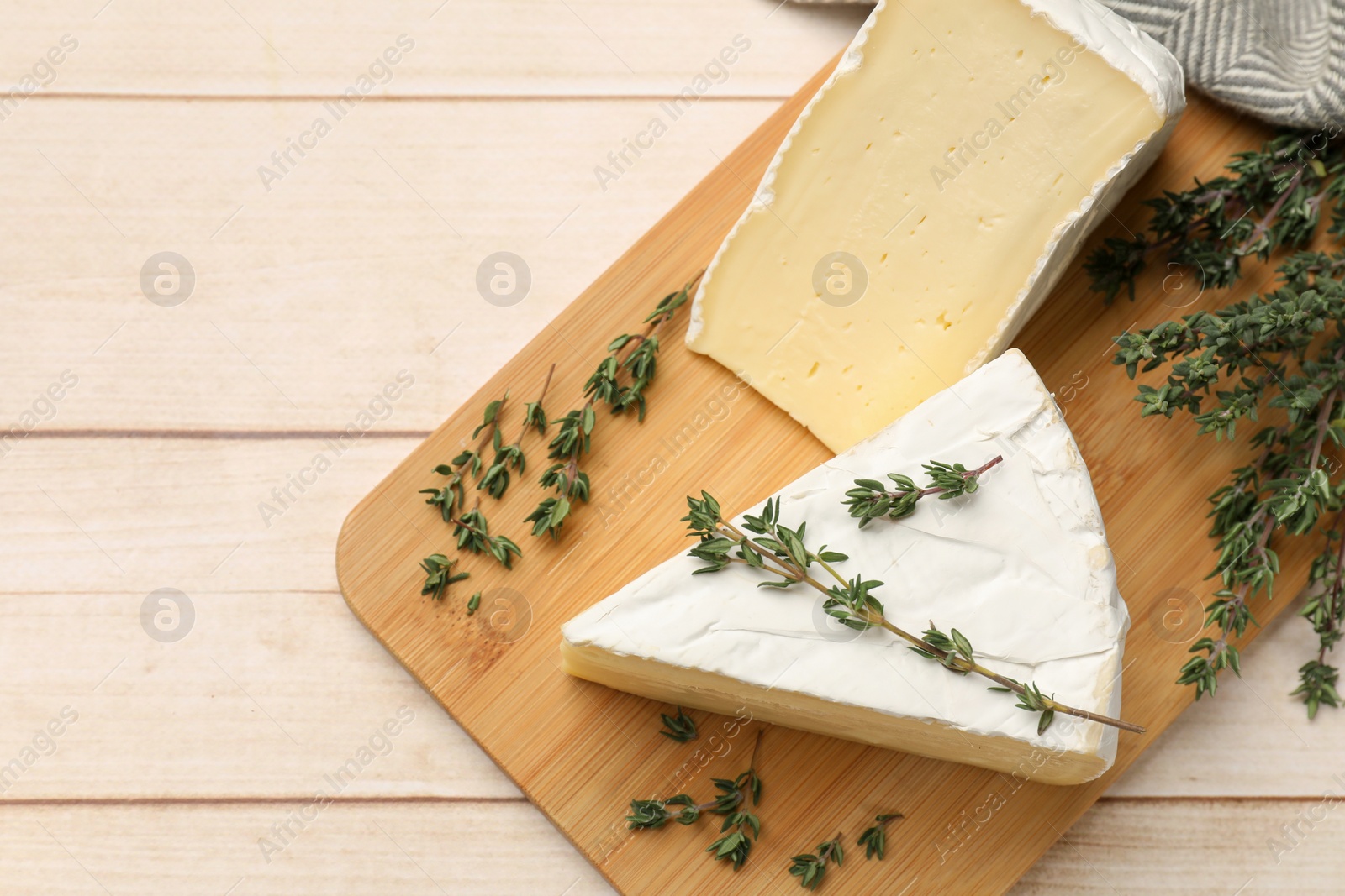 Photo of Board with pieces of tasty camembert cheese and thyme on light wooden table, top view. Space for text