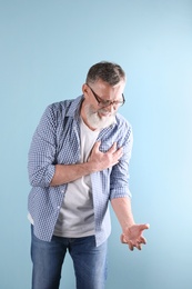 Mature man having heart attack on color background