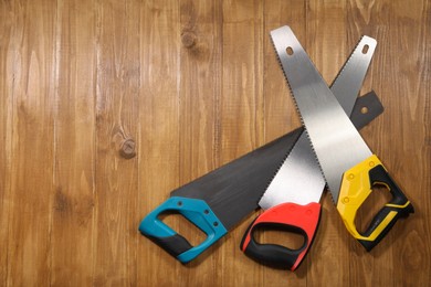 Saws with colorful handles on wooden background, flat lay. Space for text