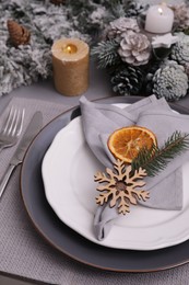 Photo of Festive place setting with beautiful dishware, fabric napkin and dried orange slice for Christmas dinner on grey table