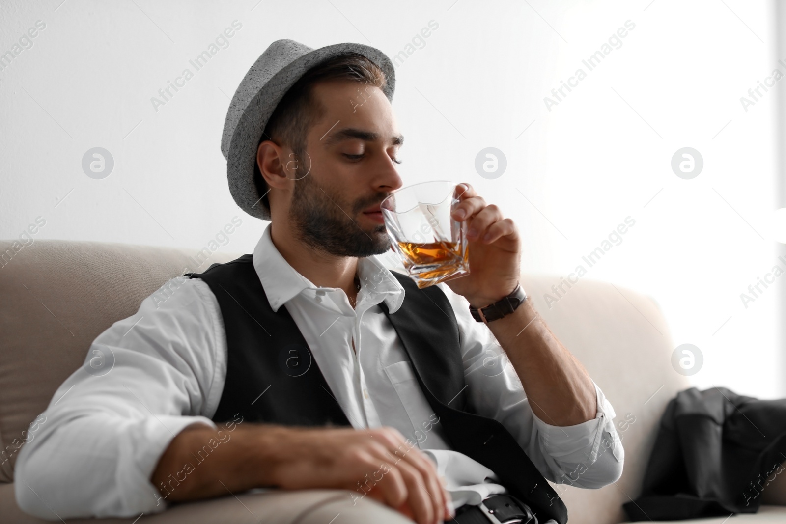 Photo of Young man with glass of whiskey sitting on sofa at home