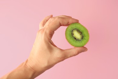 Photo of Woman holding delicious fresh kiwi on pink background, closeup