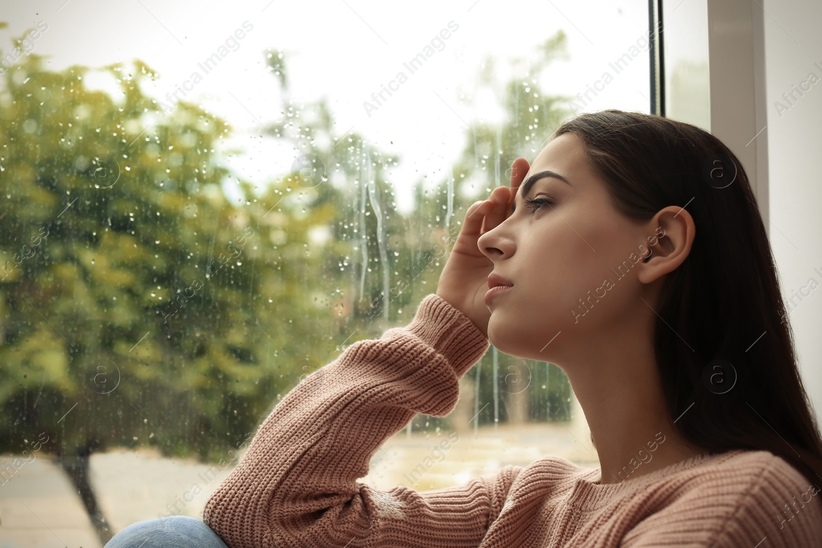 Photo of Young sad woman sitting near window at home