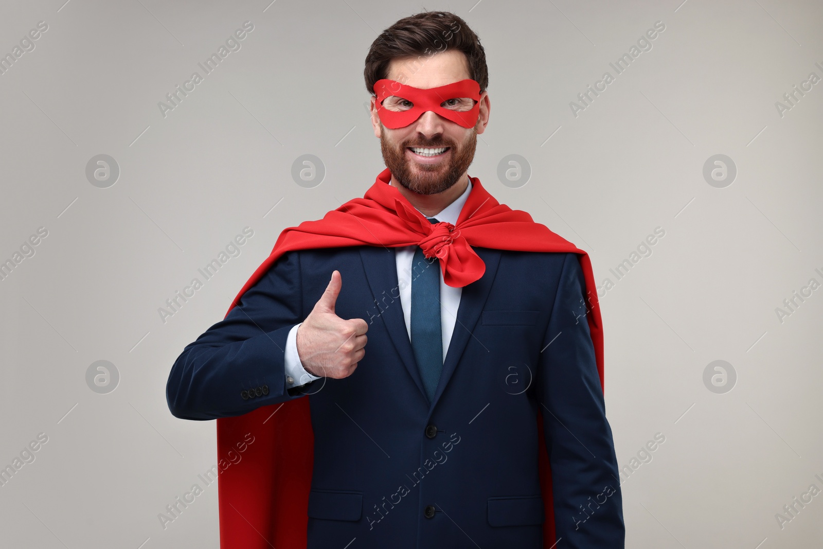 Photo of Happy businessman in red superhero cape and mask showing thumbs up on beige background