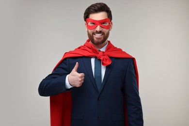 Happy businessman in red superhero cape and mask showing thumbs up on beige background