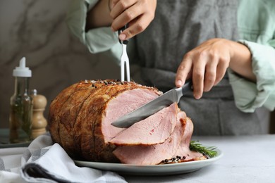 Photo of Woman cutting delicious baked ham at light grey table, closeup