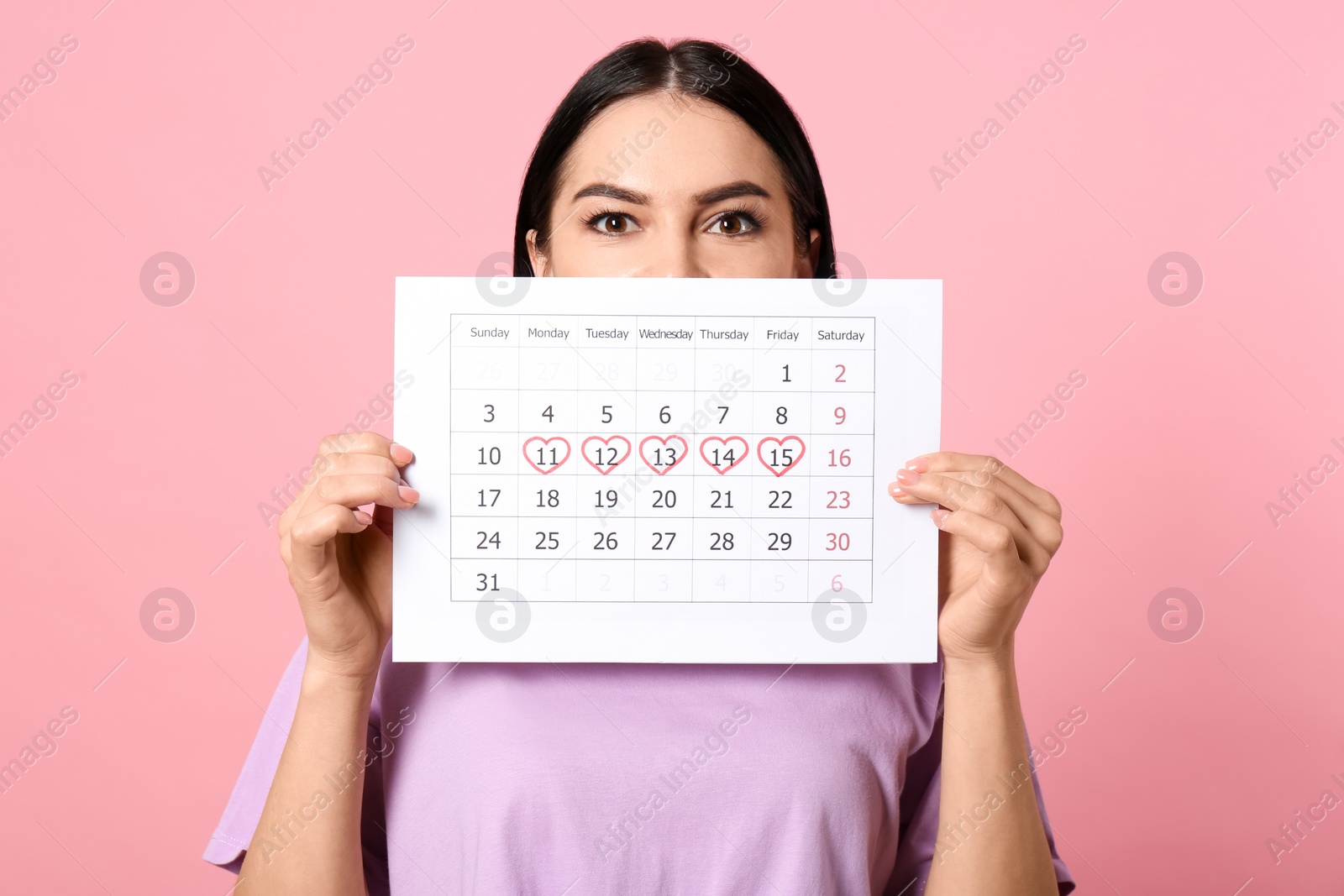 Photo of Young woman holding calendar with marked menstrual cycle days on pink background