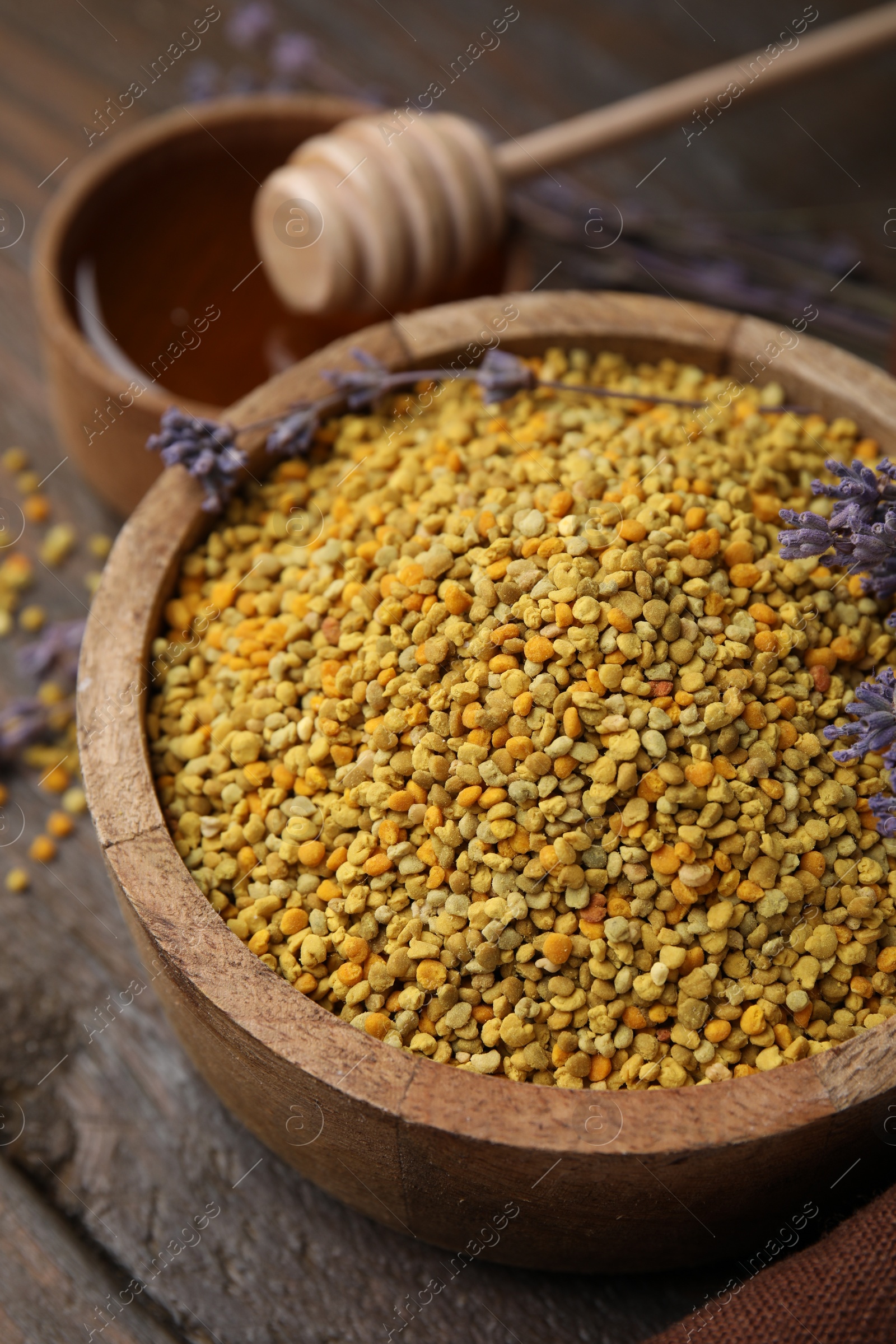 Photo of Fresh bee pollen granules in bowl and lavender on wooden table, closeup