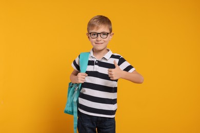 Photo of Happy schoolboy in glasses with backpack on orange background