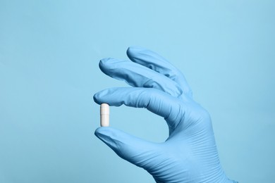 Photo of Doctor holding pill on light blue background, closeup