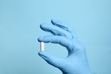 Doctor holding pill on light blue background, closeup