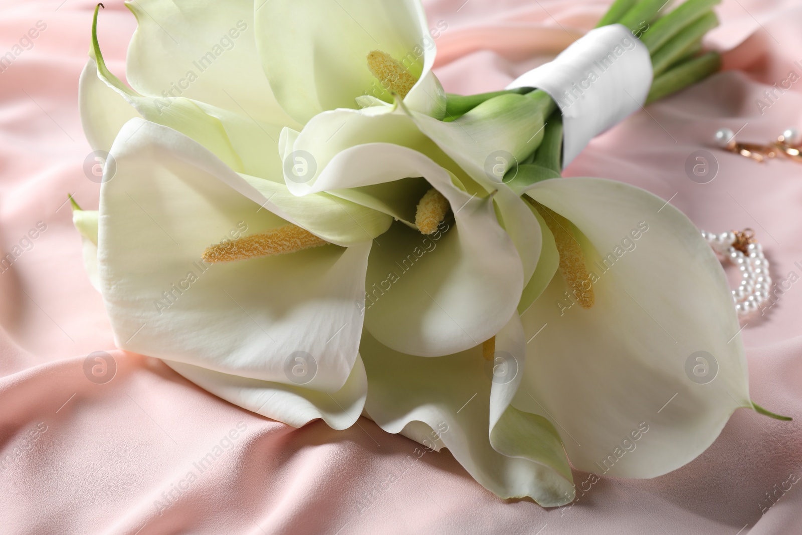 Photo of Beautiful calla lily flowers tied with ribbon on pink fabric, closeup
