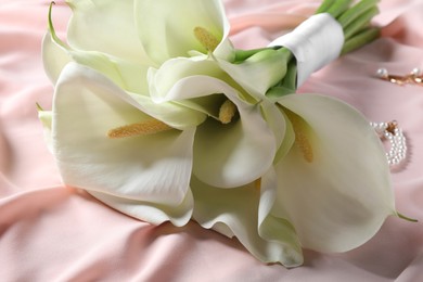 Beautiful calla lily flowers tied with ribbon on pink fabric, closeup