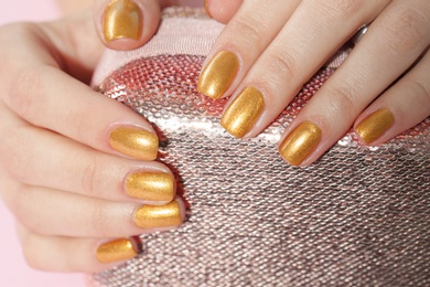 Photo of Woman holding manicured hands with golden nail polish on bag, closeup