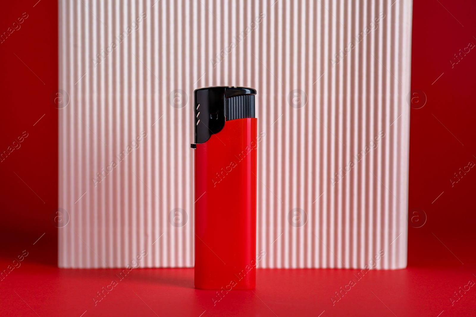 Photo of Stylish small pocket lighter and white corrugated fiberboard on red background