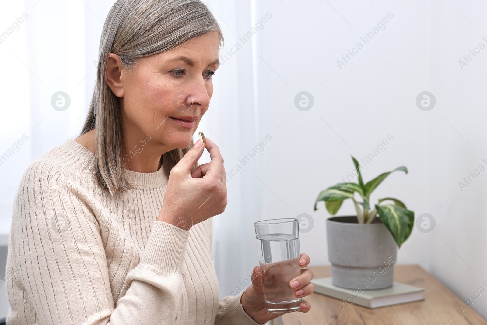 Photo of Beautiful woman taking vitamin pill at table indoors