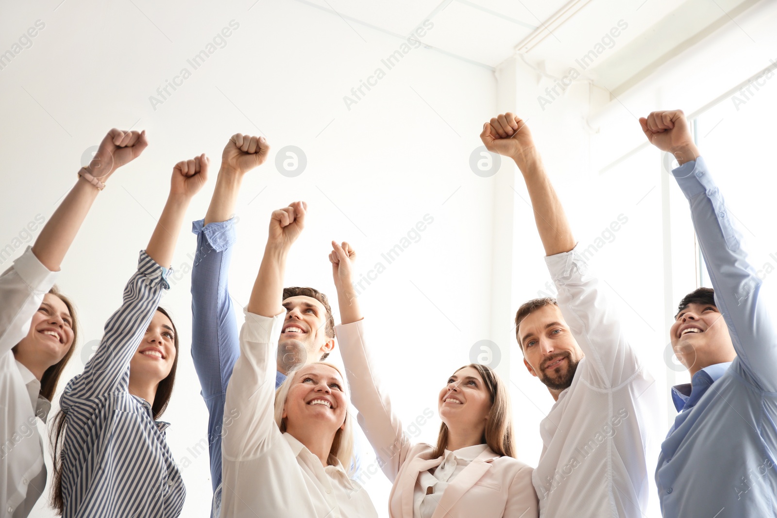 Photo of People raising fists together indoors. Unity concept
