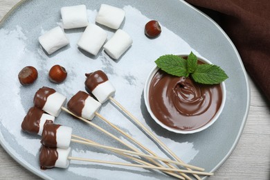 Photo of Tasty marshmallows dipped into chocolate on white wooden table, top view