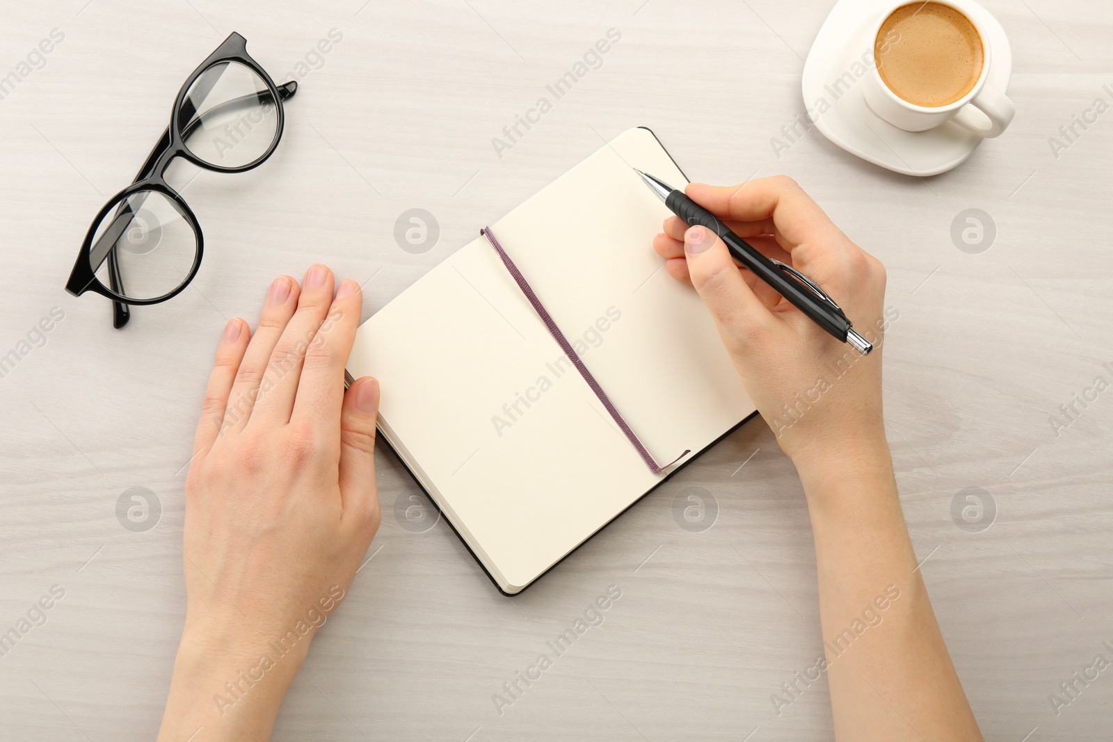 Photo of Woman writing in notebook at light wooden table, top view