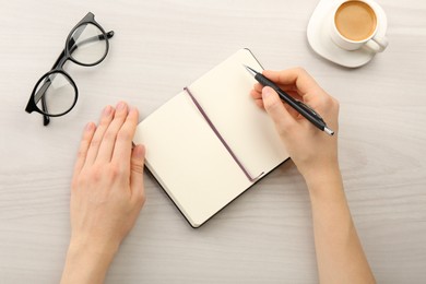 Woman writing in notebook at light wooden table, top view