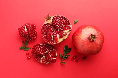 Photo of Fresh pomegranates and green leaves on red background, flat lay