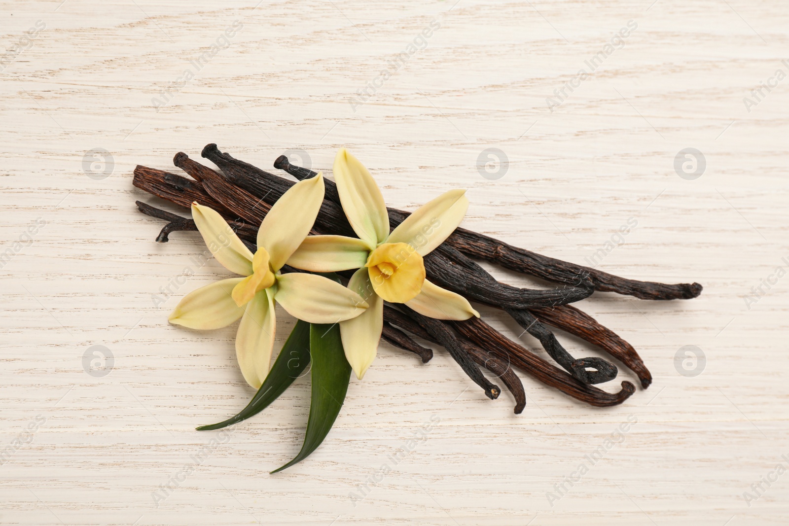 Photo of Beautiful vanilla flowers and sticks on white wooden table, flat lay