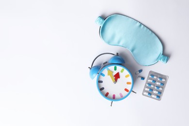 Photo of Sleeping mask, pills and alarm clock on white background, flat lay. Insomnia treatment