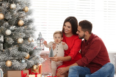 Happy family with cute baby near Christmas tree at home