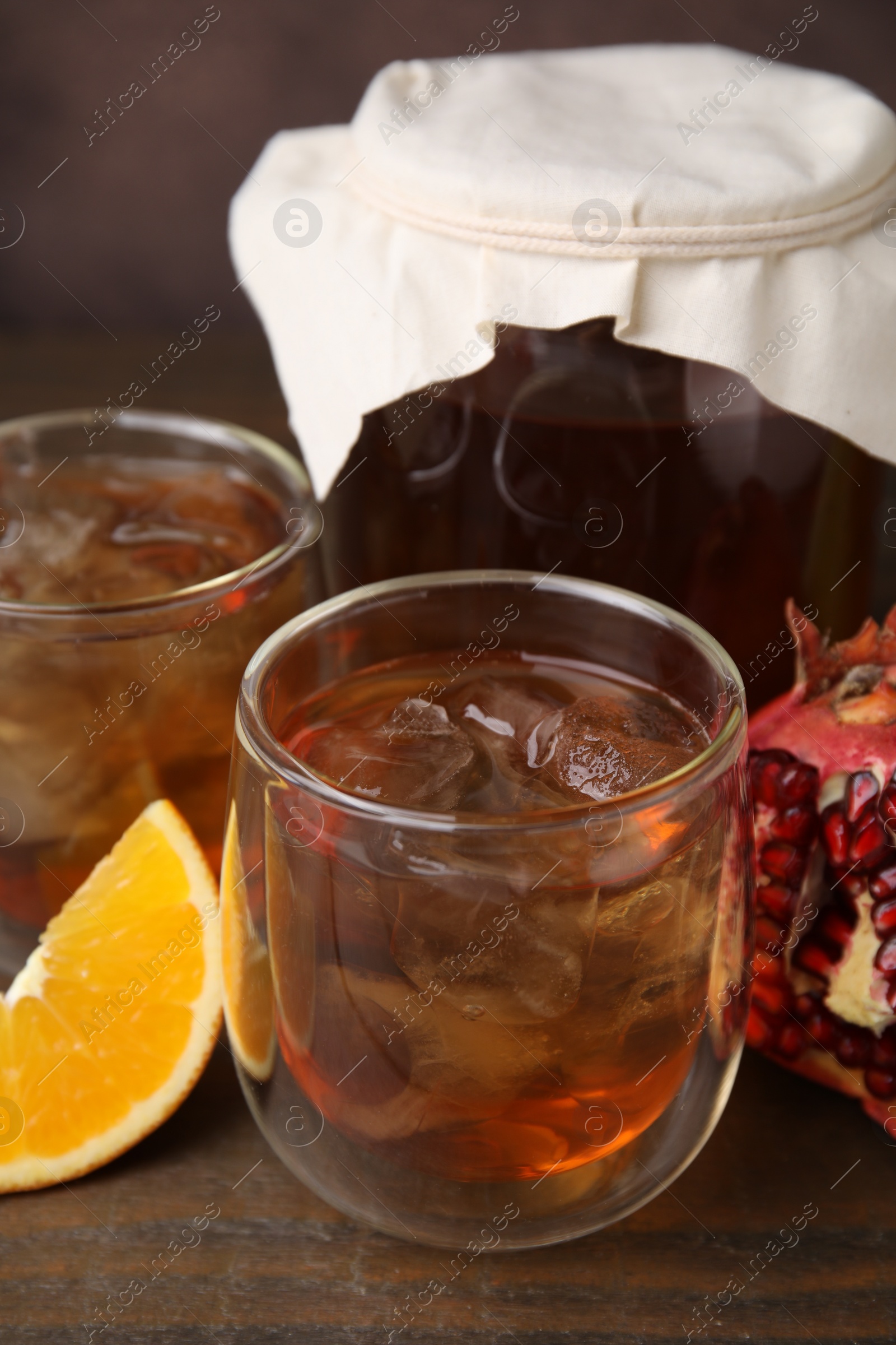 Photo of Tasty kombucha with ice cubes and fruits on wooden table