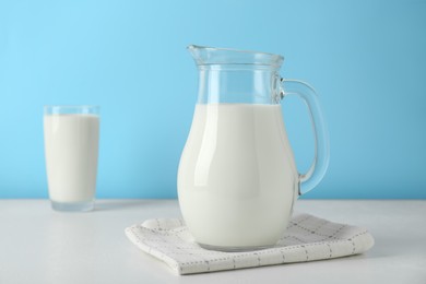 Photo of Jug of fresh milk on white table against light blue background