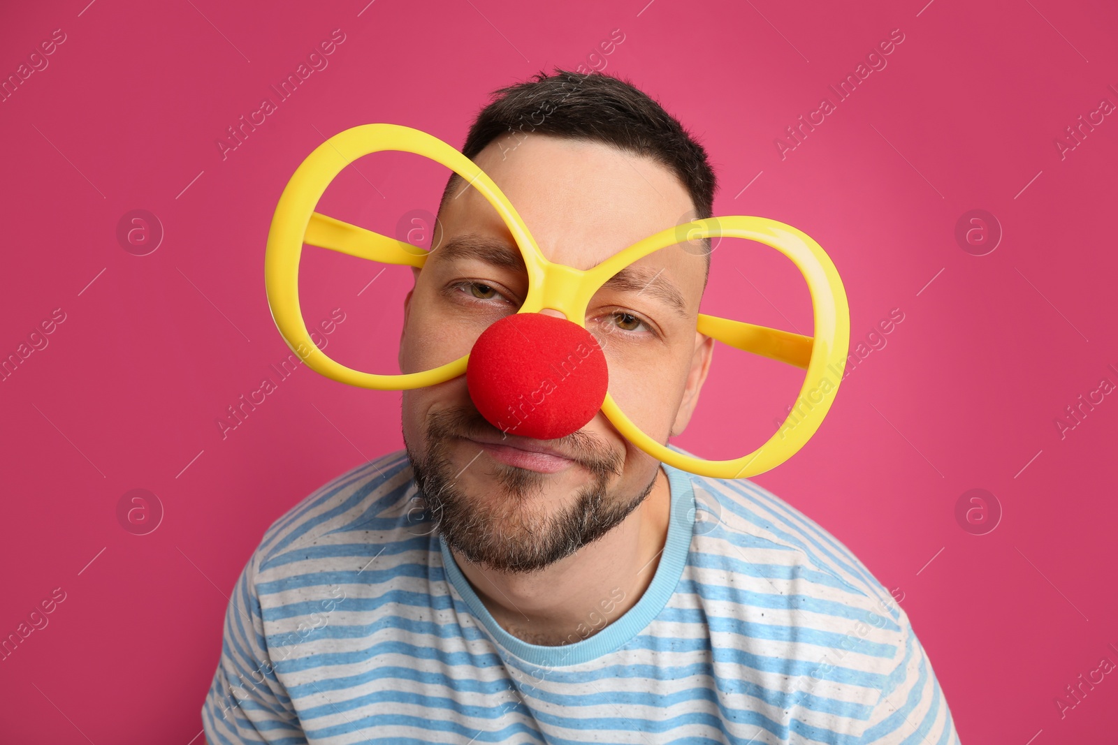 Photo of Emotional man with large glasses and clown nose on pink background. April fool's day