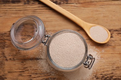 Glass jar and spoon with active dry yeast on wooden table, flat lay