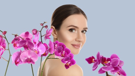 Beautiful young woman and orchid flowers on light background. Spa portrait