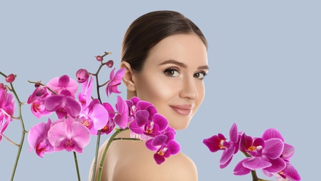 Image of Beautiful young woman and orchid flowers on light background. Spa portrait