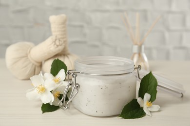 Photo of Jar of salt scrub and beautiful jasmine flowers on white wooden table