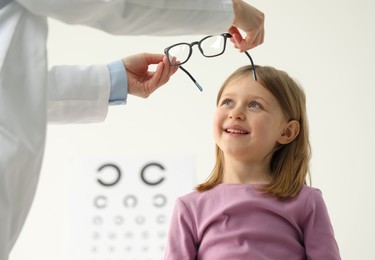 Vision testing. Ophthalmologist giving glasses to little girl indoors, low angle view