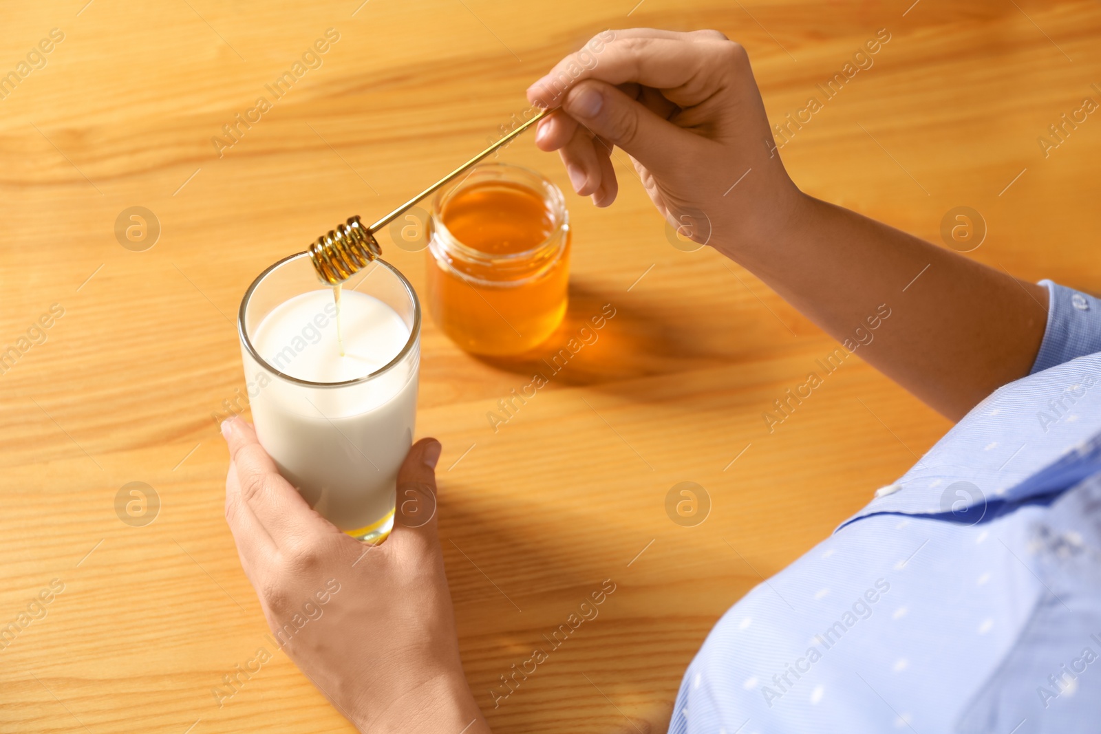 Photo of Woman adding honey to milk at table, closeup